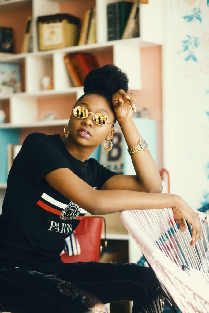 Black girl with golden sunglasses and sun reflection looking towards the camera with a black shirt