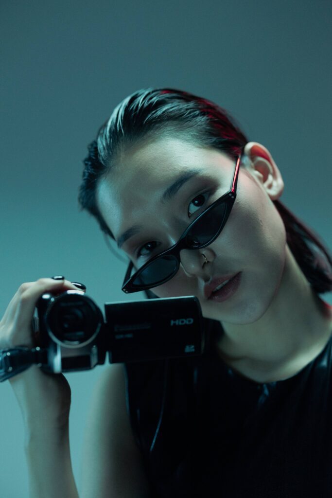 Asian girl wearing black minimalistic sunglasses for women while holding a camera