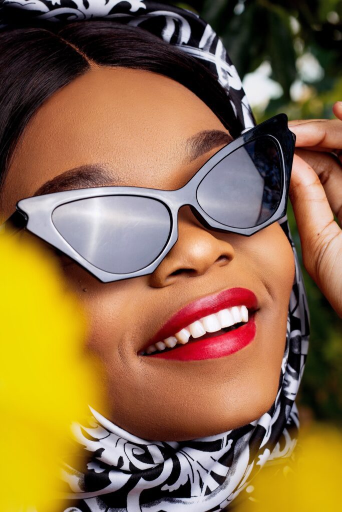 Black woman wearing cat eye sunglasses which matches her diamond face shape with a luxurious black and white scarf