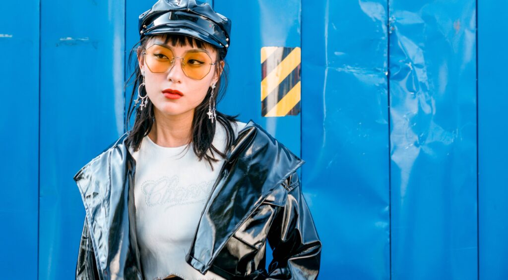 Asian girl wearing oversized coloured sunglasses while wearing a leather jacket and a baret
