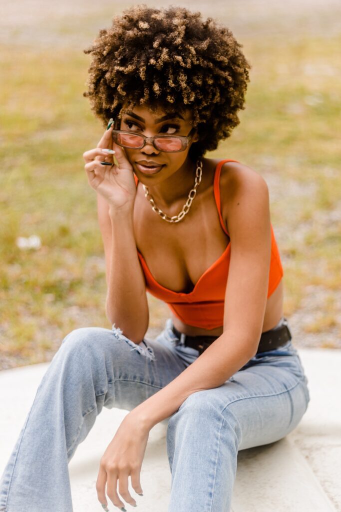 black girl with curly hair wearing red retro sunglasses for women while sitting in the park