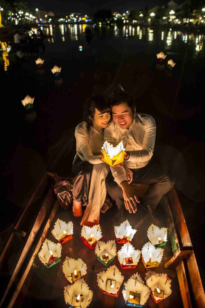 Asian woman dressed for her date night with her boyfriend next to her, both in a white outfit on a boat surrounded with romantic candles